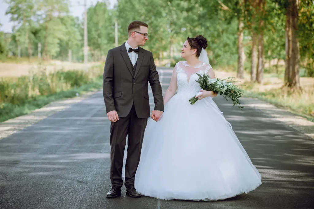 Az ifjú pár kézen fogva sétál a kertben, a menyasszony bő szoknyás fehér ruhájában.