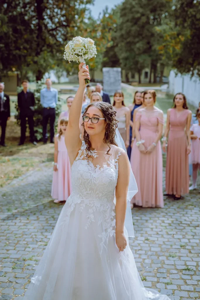 Csokordobás pillanata a menyasszonnyal és a mögötte várakozó vendégekkel.